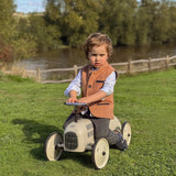 Boy wearing Little Darzi wool gilet in Coral Red sitting on toy car