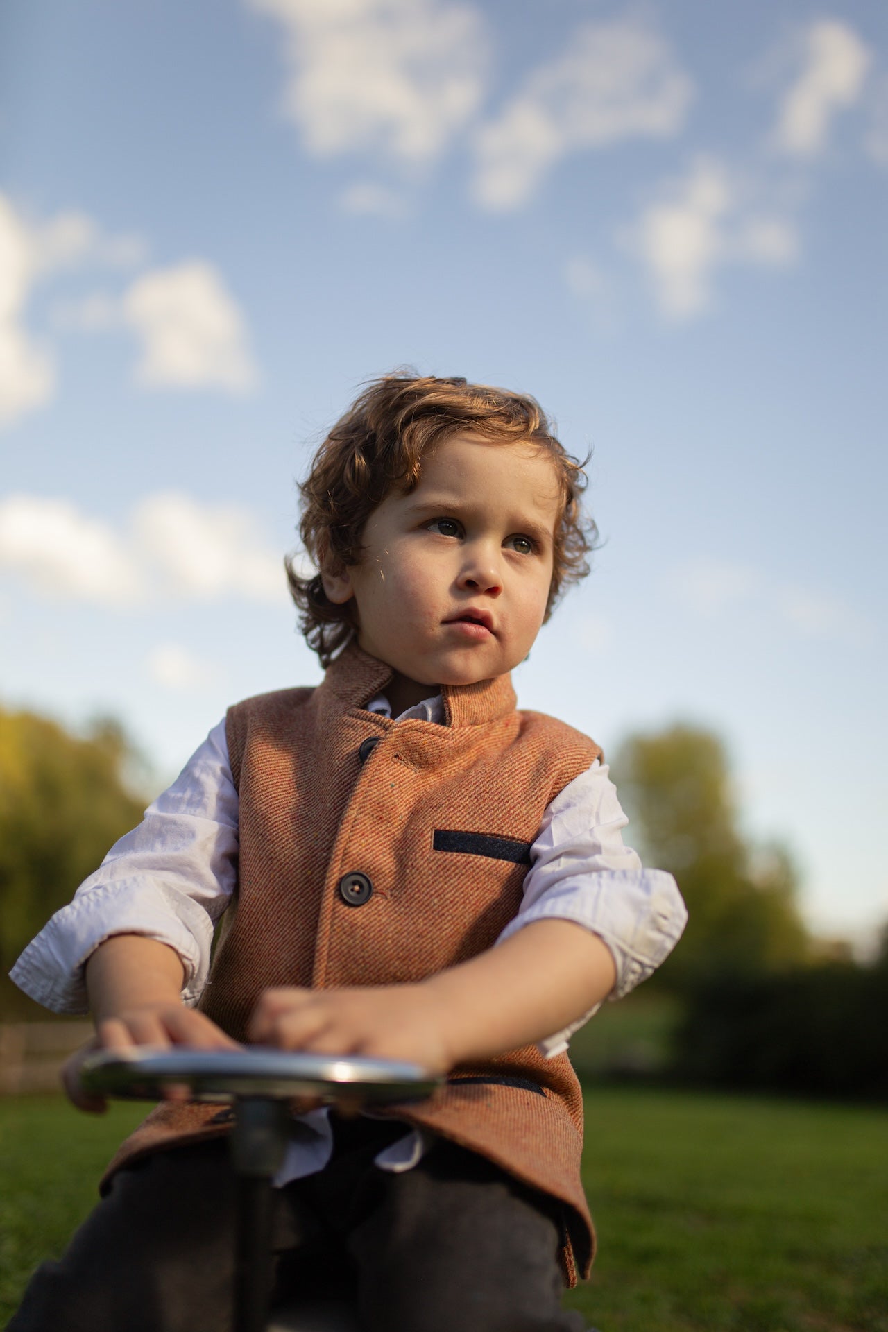 Boy wearing Little Darzi in Coral Red sitting on toy car